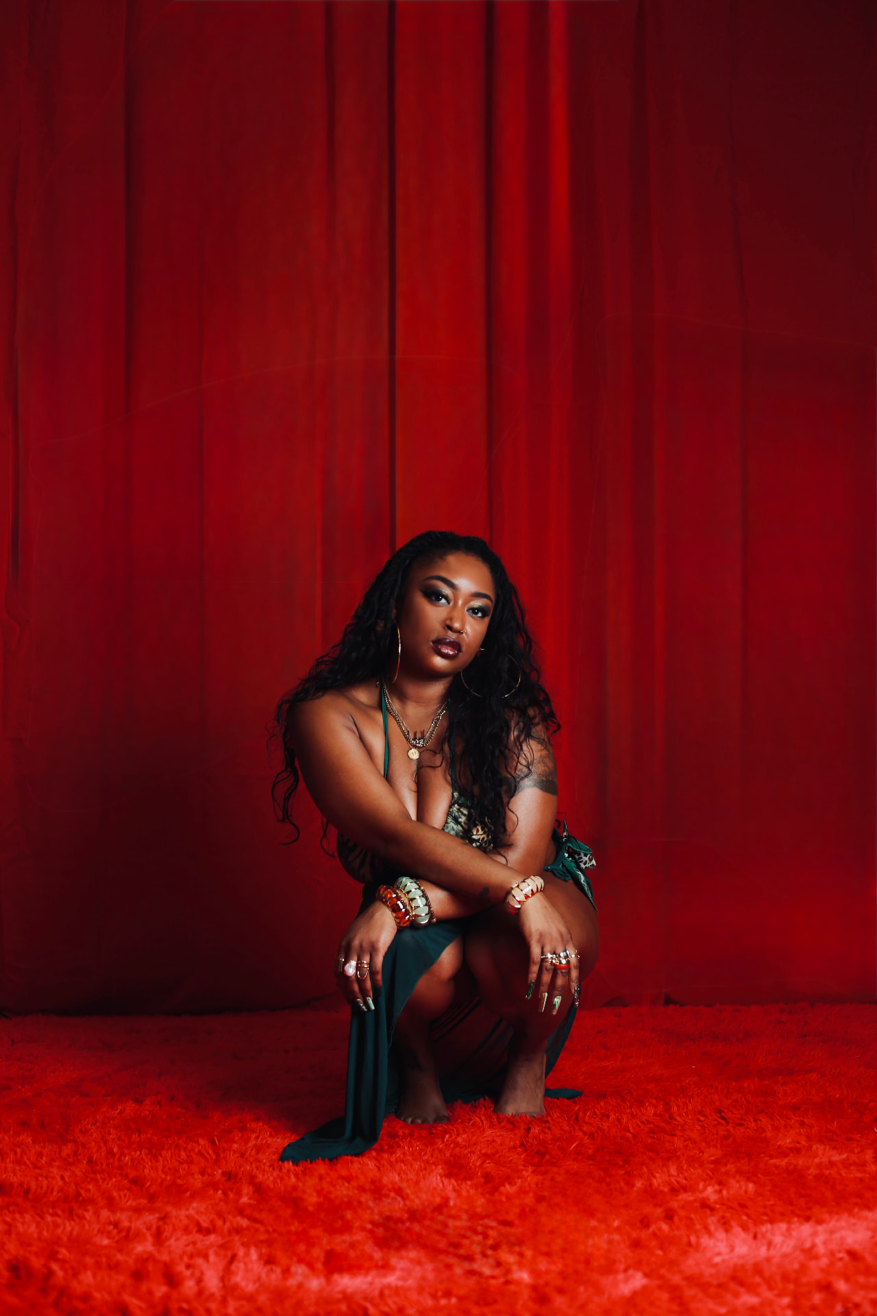 Emani, Neo-Soul and R&B singer, crouched before a deep red velvet backdrop in a green gown